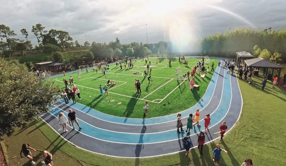 An aerial view of families on the sports field and track at the Fall Harvest Festival, with a rainbow over the trees