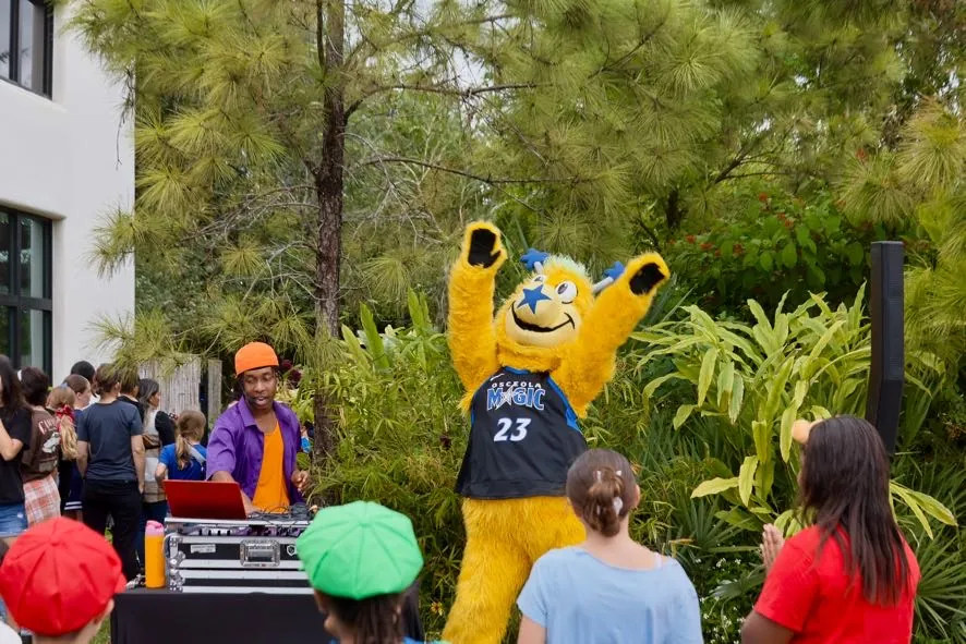The festival DJ dancing with the Osceola Magic mascot as children watch