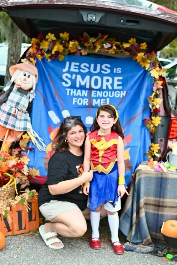 A parent and child at a Trunk or Treat car decorated with the words Jesus is s'more than enough for me