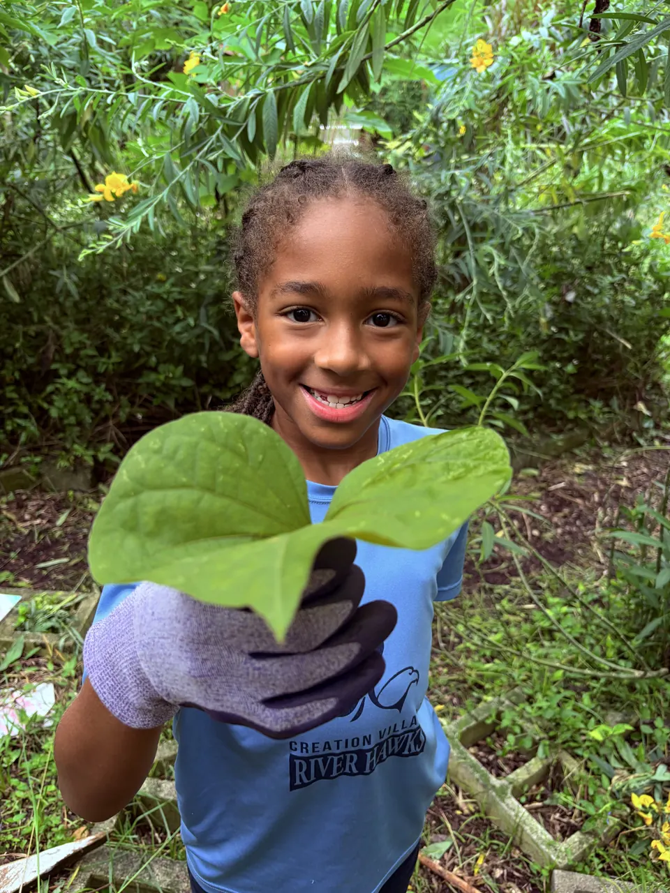 A smiling student holding up a leaf from the food forest