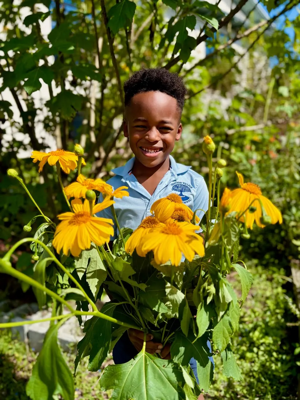 A primary student smiling among sunflowers in the school garden